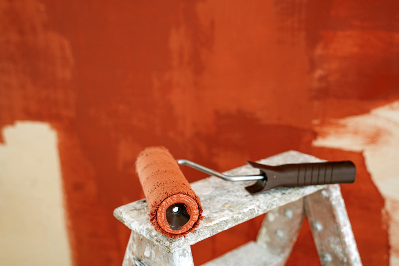 A paint-roller covered with paint on a stepladder with a wall in the background