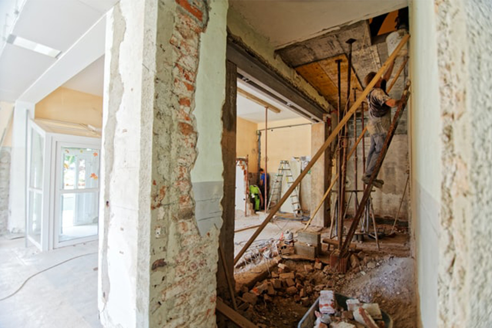 A man on the ladder in the corner of a room with demolished walls